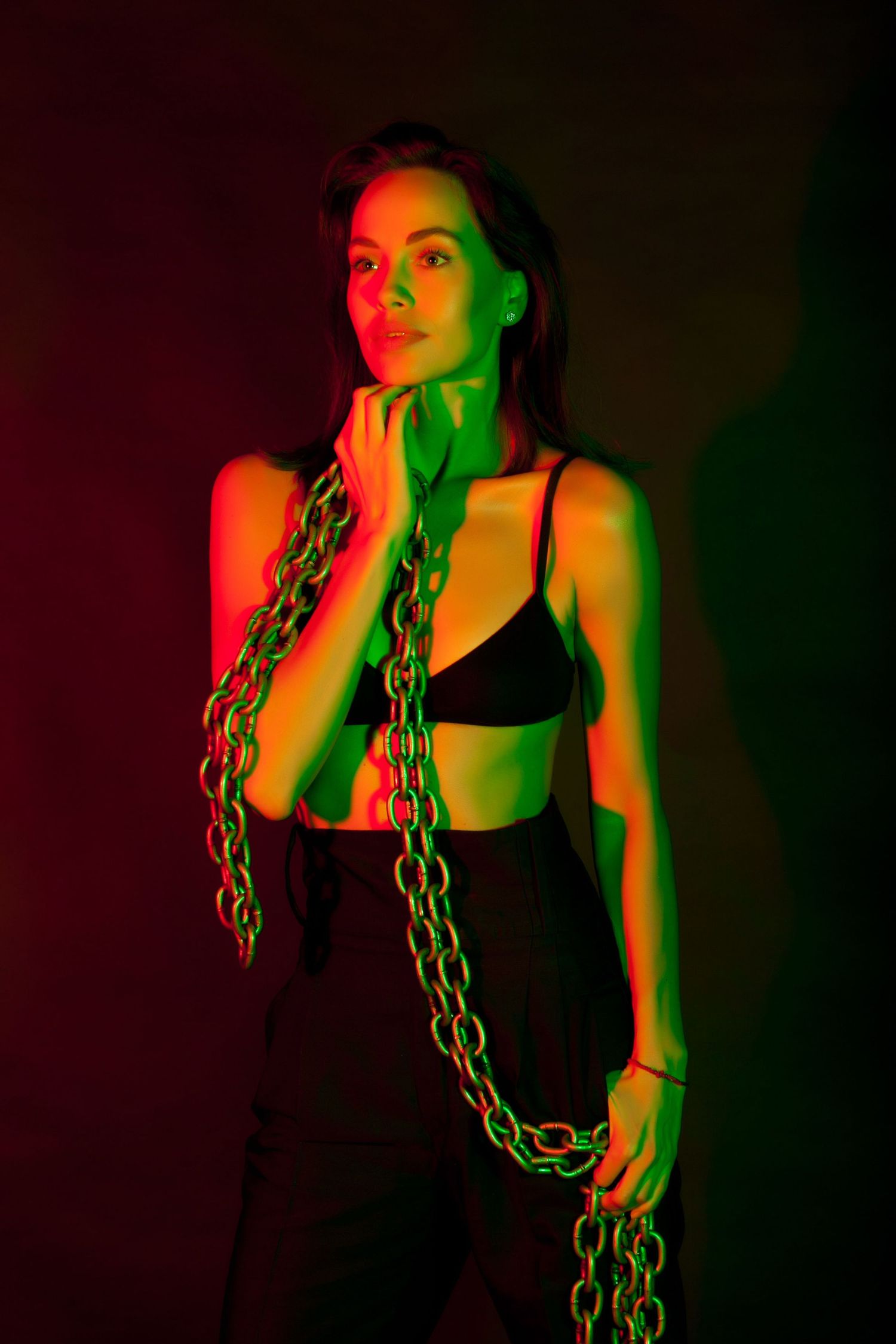 Artistic portrait with neon lighting and chains creating dramatic red and green effects.