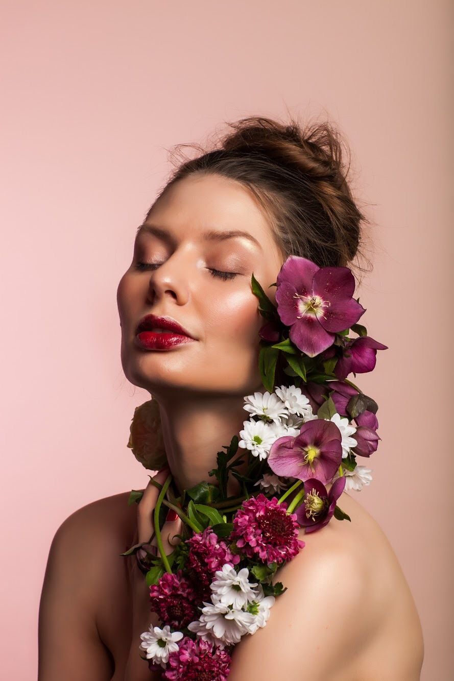 Artistic beauty portrait featuring vibrant purple and white flowers cascading along the side against a pink backdrop.