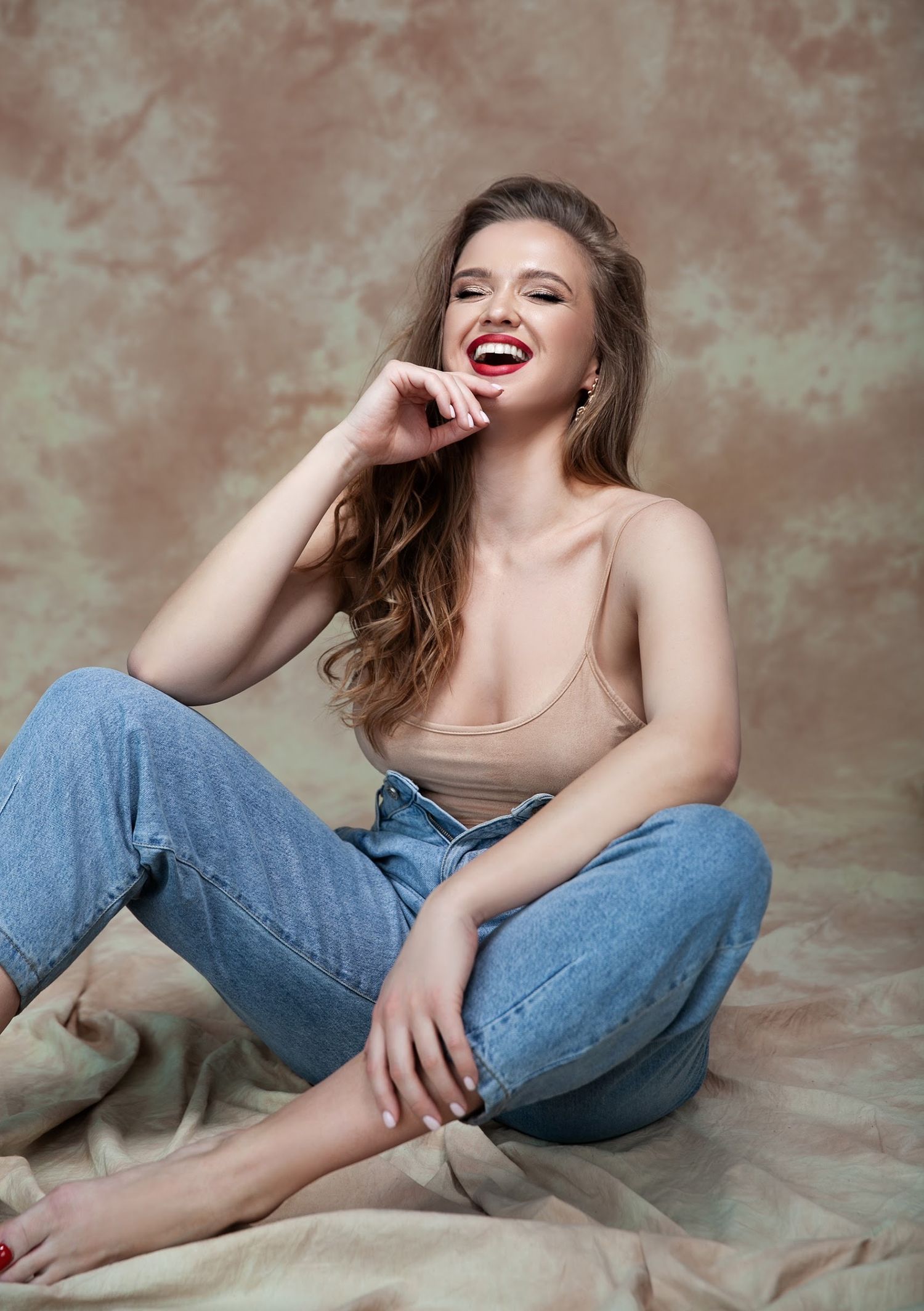 Casual portrait of person in jeans and tank top laughing on textured backdrop.