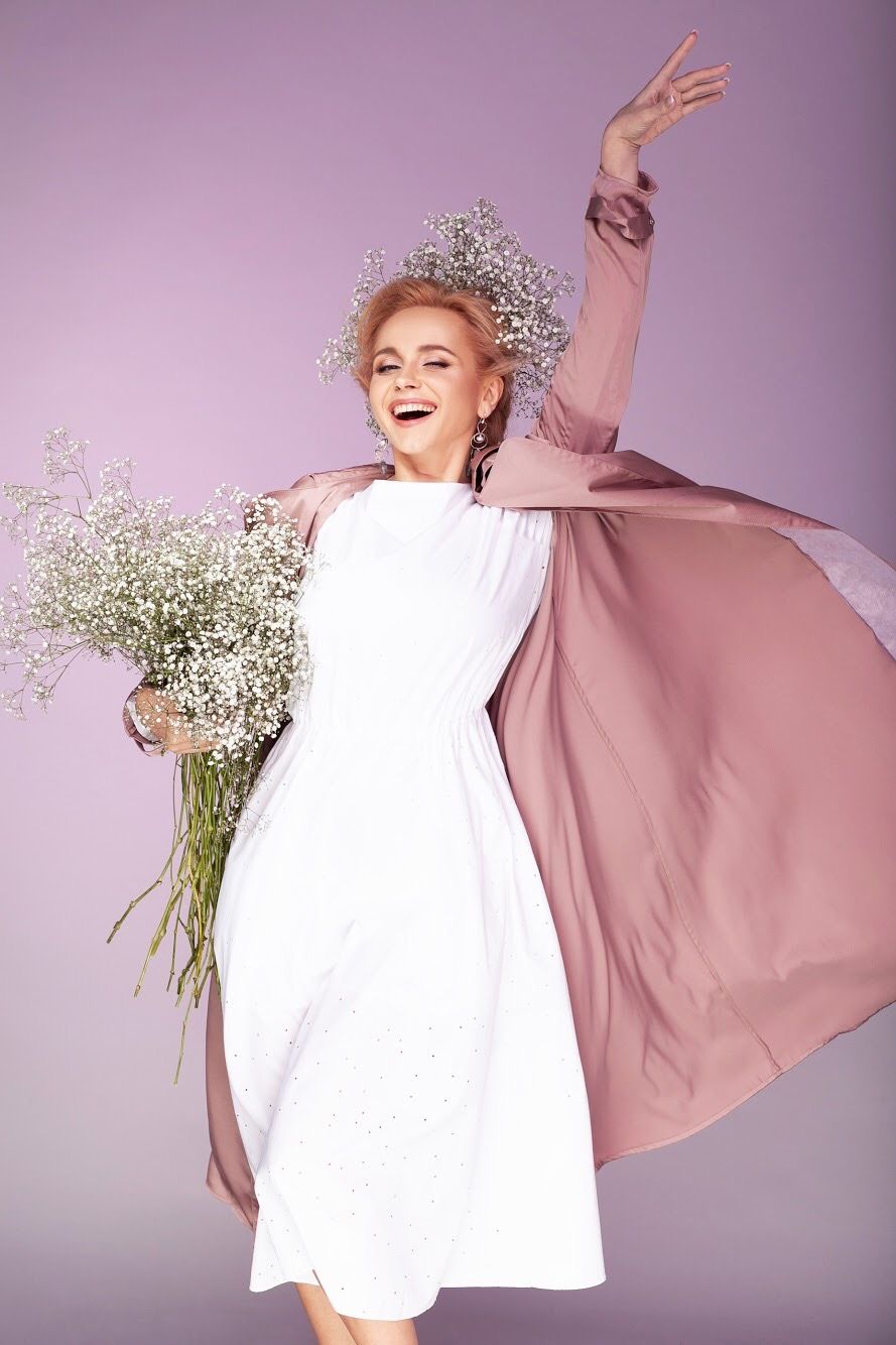 Joyful woman in white dress and pink cape holding baby's breath bouquet.