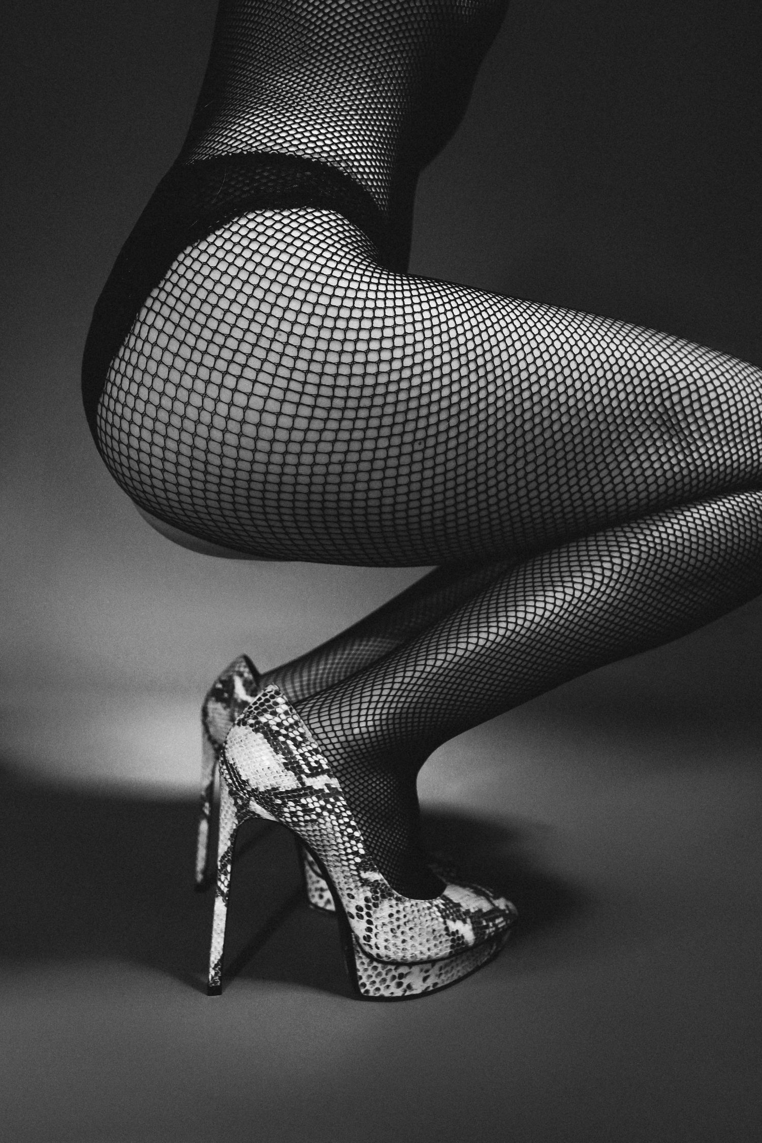 Close-up of legs in fishnet stockings and snakeskin print high heels.