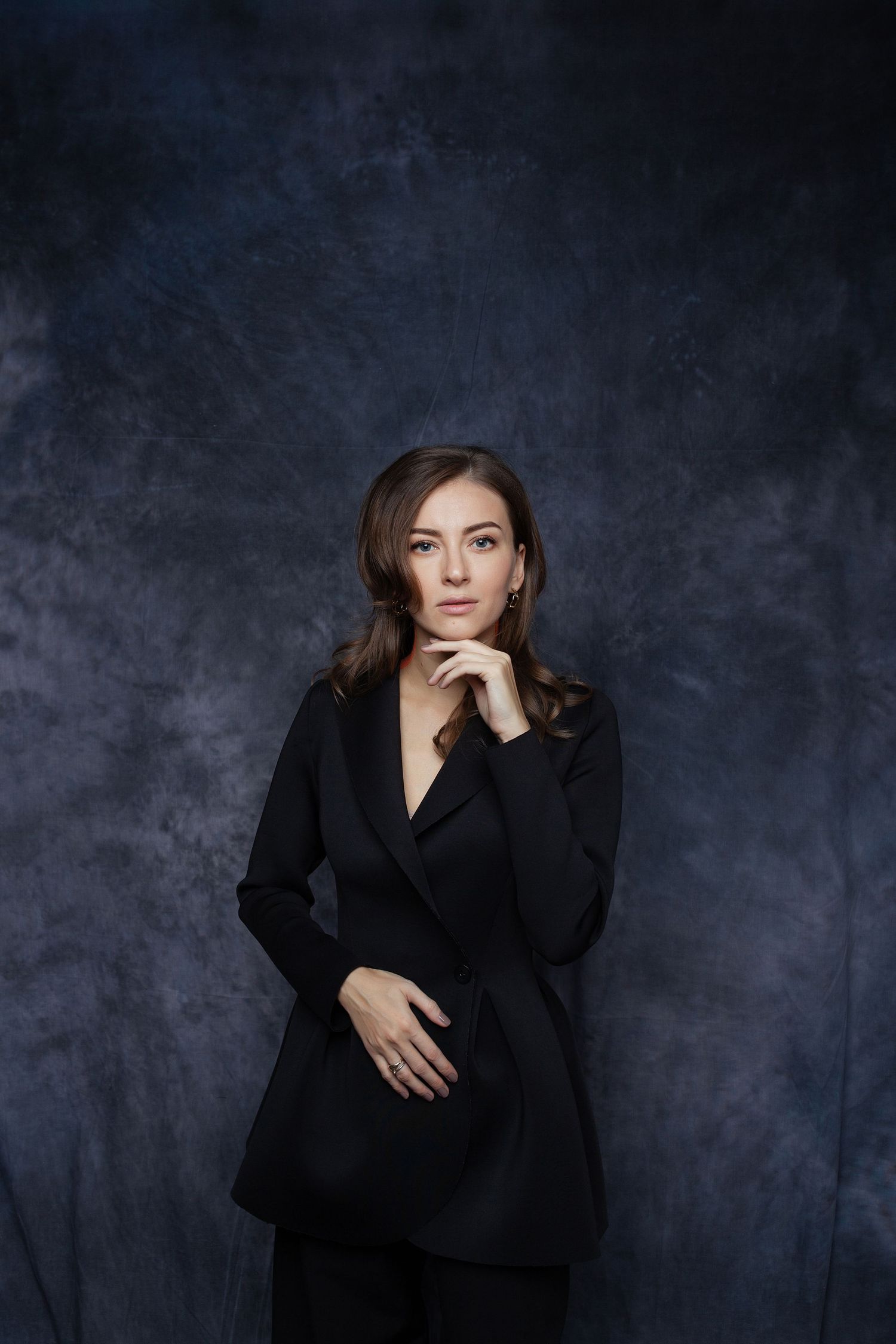 Elegant fashion portrait in black blazer against textured dark gray studio background.