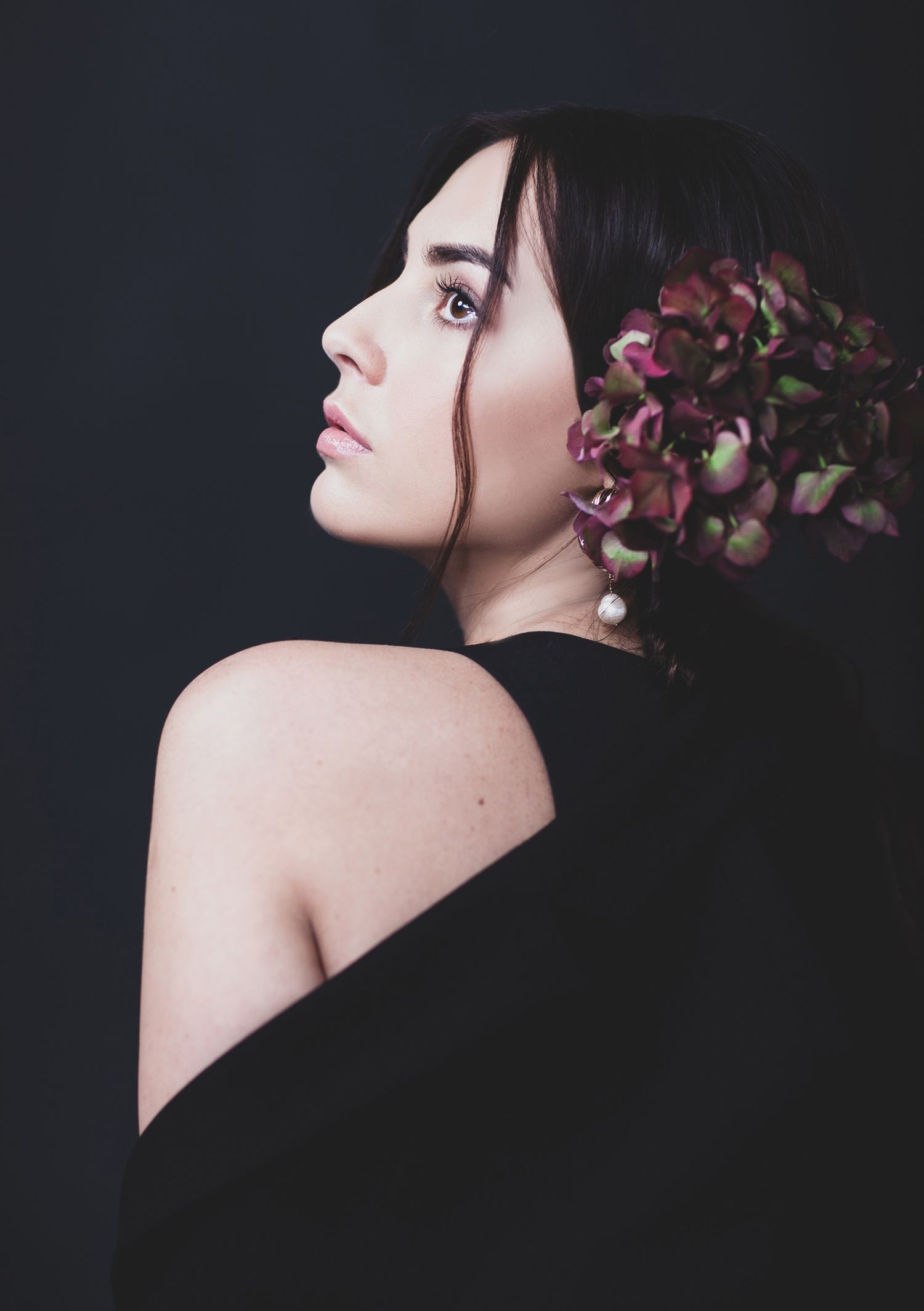 Artistic side profile portrait with pink flowers against dark background.