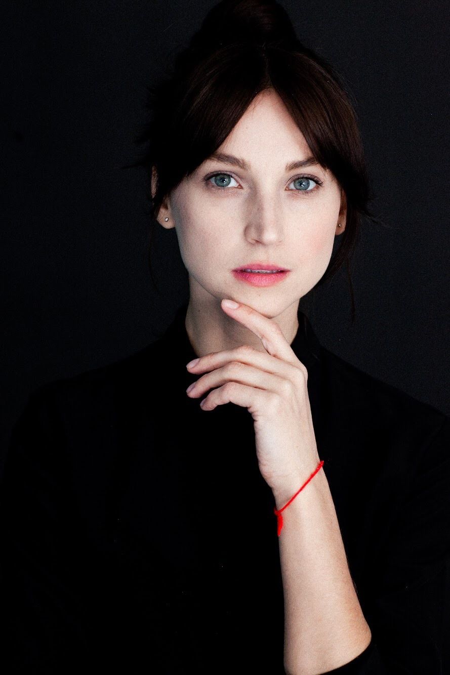 Elegant portrait with hand posed under chin wearing black top against dark background.
