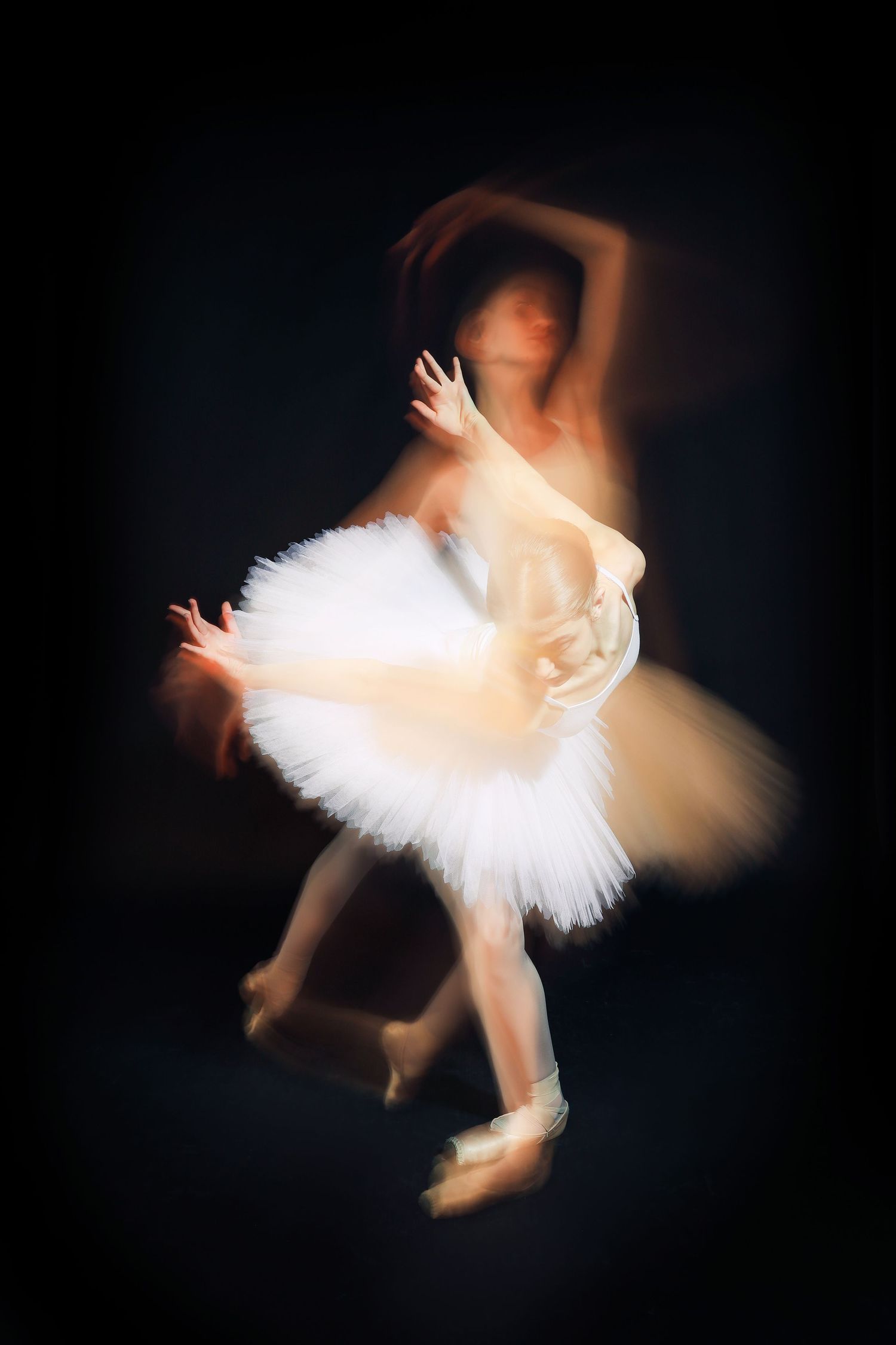 Motion-blurred image of ballet dancer in white tutu performing against dark background.