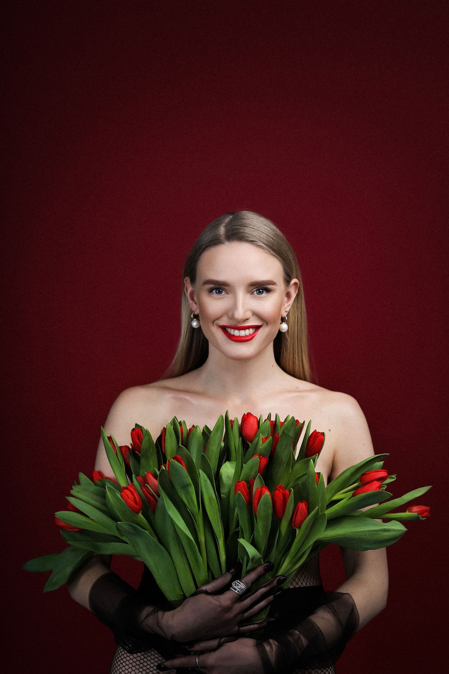 Elegant portrait with red tulips and black gloves against burgundy background.