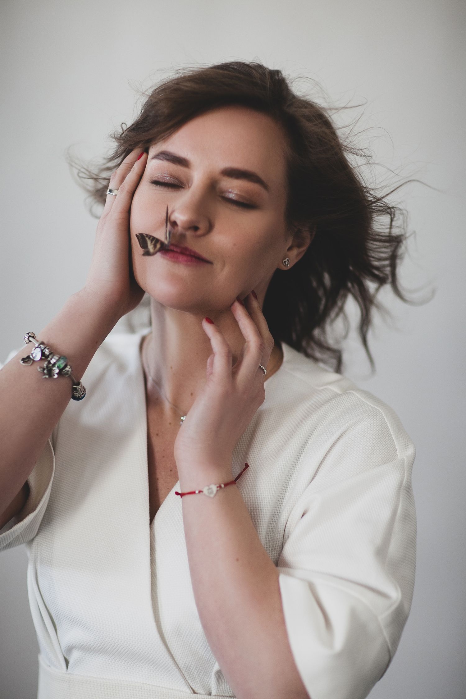 Artistic portrait of person in white with windswept hair touching their face with delicate jewelry.