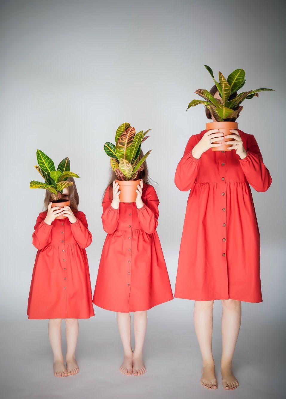 Conceptual photo of three figures in red dresses holding plants in ascending height order.