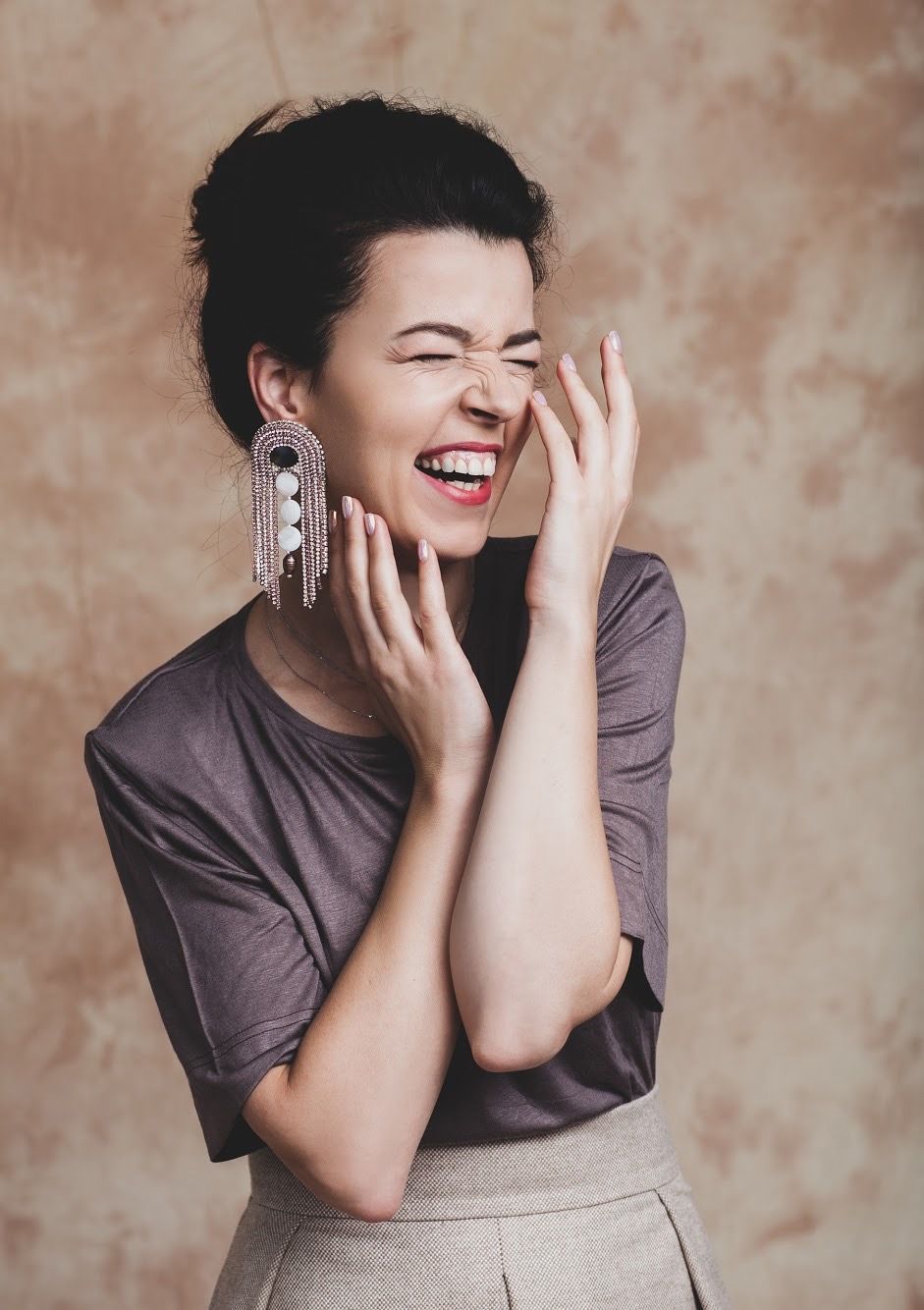 Expressive portrait of person laughing with statement earrings against neutral background.