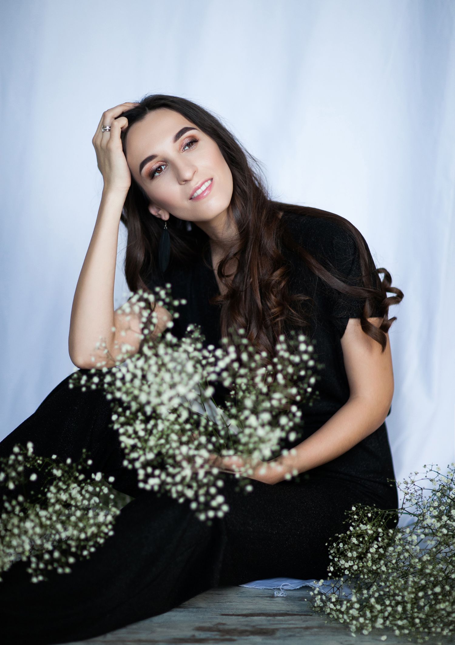 Studio portrait with baby's breath flowers featuring black dress against light blue backdrop.