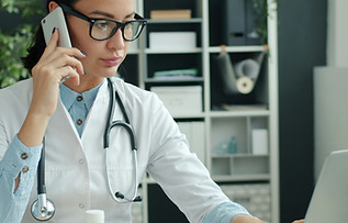 Young female doctor is talking on mobile phone and using laptop computer working in office