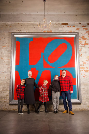 Family of 5 wearing black and red checkers in front of LOVE portrait. 