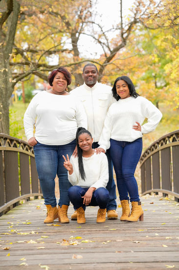 Family of 4 wearing white tops and denim and standing together on a bridge