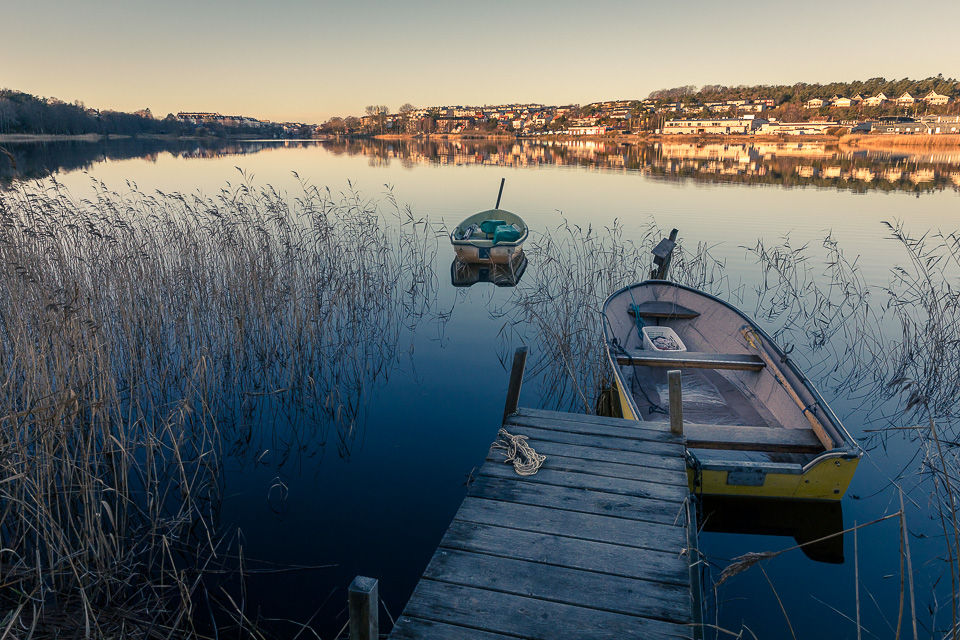 To robåter ved liten brygge med stille vann