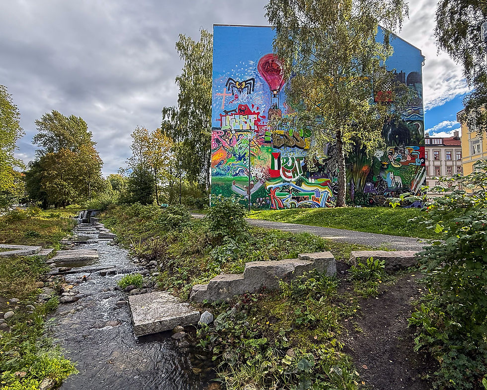 Liten bekk Hovindbekken med fasade med veggmaleri ved siden av i Oslo