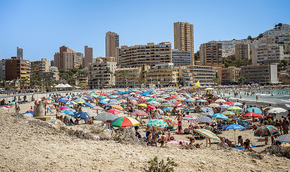 Sandstrand med mange parasoller og badegjester med høyhus i bakgrunnen ved Cala Finestrat/Cala Villajoyosa i Villajoyosa på Costa Blanca