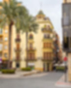 Gammel gul murbygning i by med palmer foran nær Centro Historico de Elche