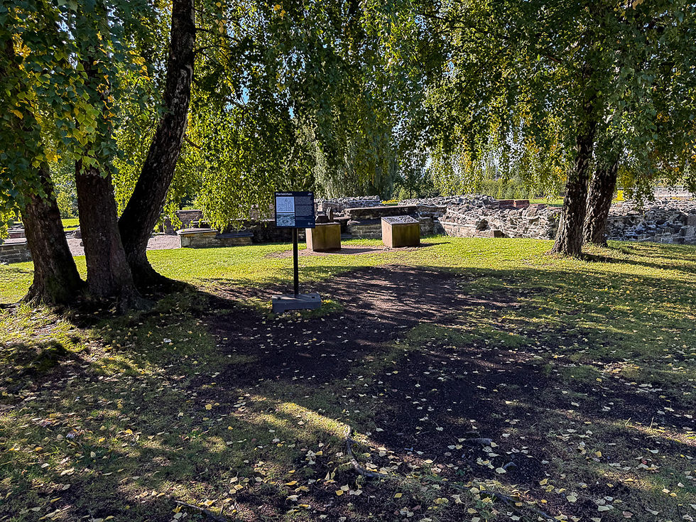 Informasjonsplakat under trekroner ved kirkeruinene ved Middelalderparken i Oslo