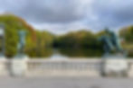 To skulpturer på bro ved dam og løvtrær i bakgrunnen i Vigelandsparken i Oslo