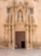 Kvinner sitter foran høy inngangsdør på vakkert dekorert fasade til Basilica de Santa Maria i Alicante gamleby