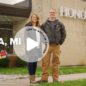 Couple standing in front of an Honor Credit Union building with the text "Baroda, MI" next to them.