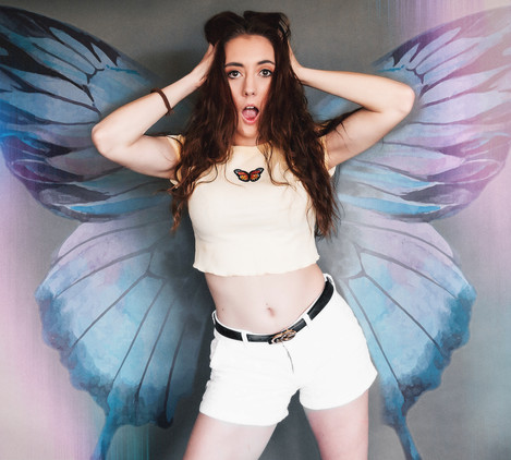 Beautiful model from Florida, Madison Masterson, wearing shirt with butterfly and white shorts. Butterfly wings are edited in the photo. She is making a surprised face and holding her hair with her hands.