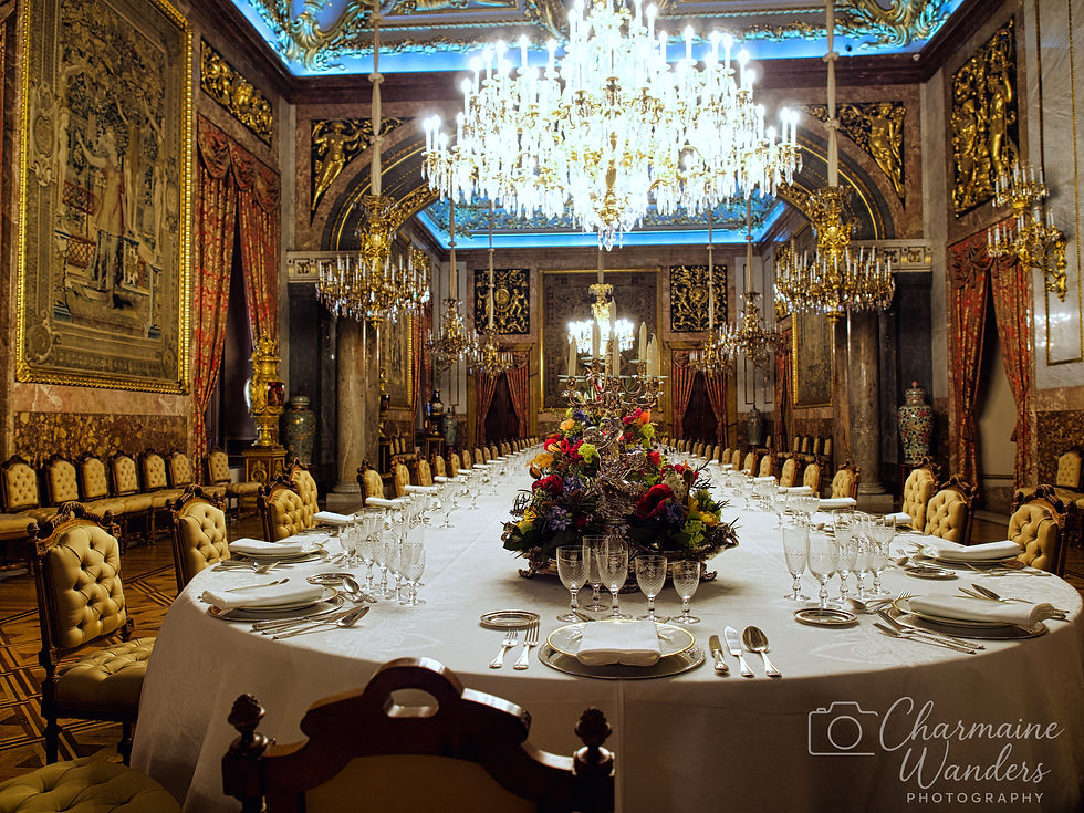 Lavish dining room with long, elegantly set table, ornate chandeliers, and rich decorations. A grand, opulent atmosphere prevails.