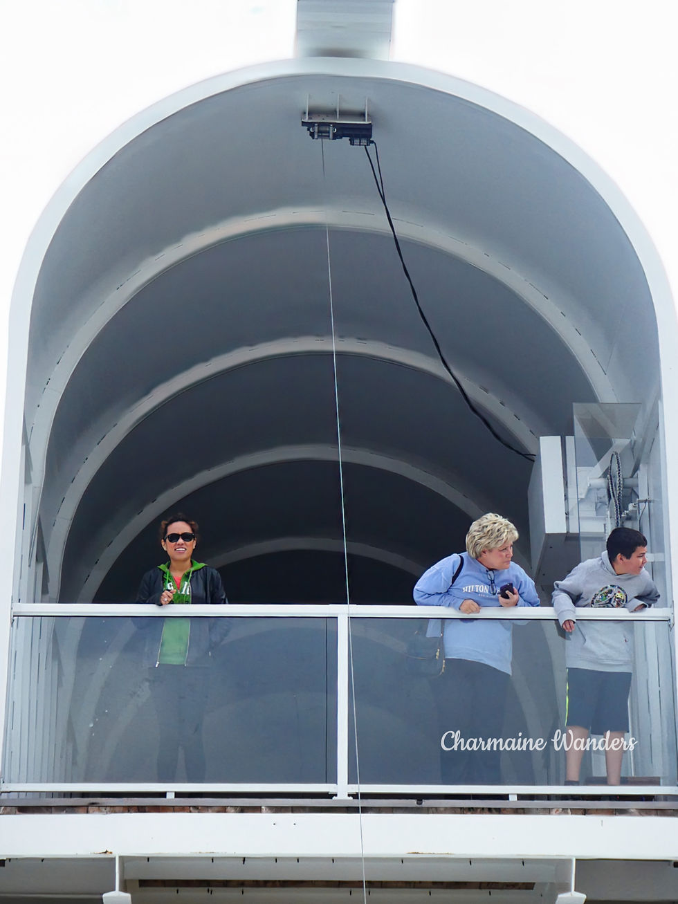 Charmaine inside a giant mailbox with 2 other people; two look out, Charmaine smiles at the camera. The background features a white arched structure.