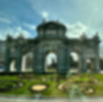 L'arc en pierre décorative avec trois arcs se tient sous un ciel bleu. Entouré de jardins en houpon et de bâtiments de la ville. Le texte latin décore l'arc.