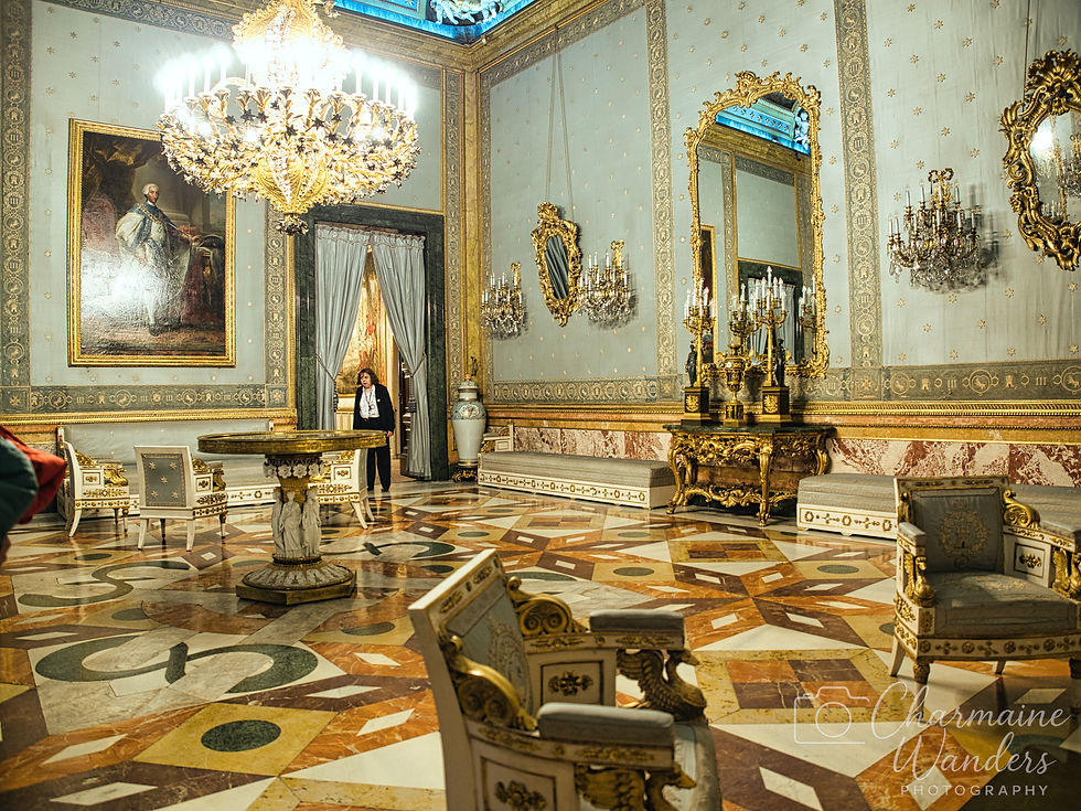 Elegant room with lavish decor, large chandelier, ornate mirrors, and a marble floor. A person stands near a door, creating a regal atmosphere.
