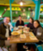 Quatre personnes prennent une table dans un restaurant de couleur, souriant de pâtes et de boissons. Décor vert et jaune, une atmosphère confortable.