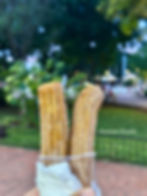 Chichen Itza Day Trip from Cancun Two sugar-coated churros in a cup held by hand, with a park and trees blurred in the background. Text reads "Charmaine Wanders".