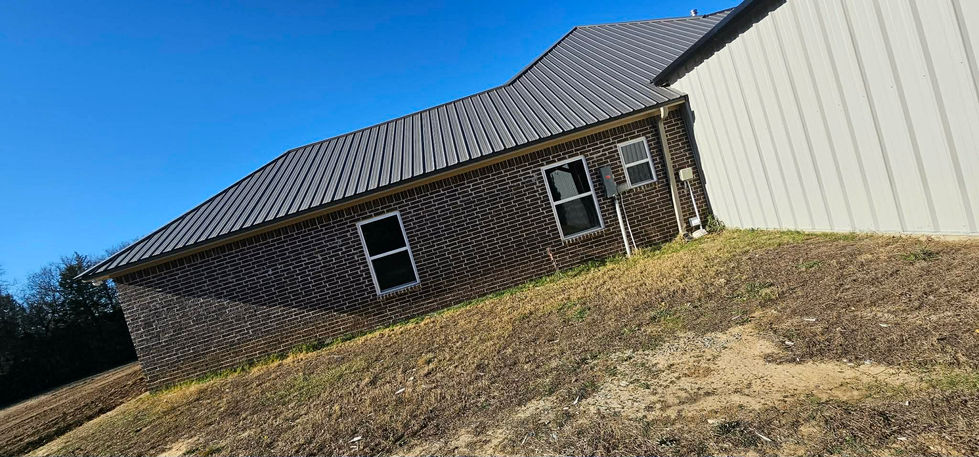 New house with dark brick, metal roof, light siding on grassy slope.