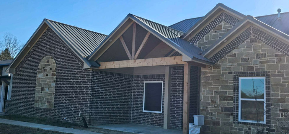 Exterior of new building with dark brick, stone, metal roof, gabled entrance.