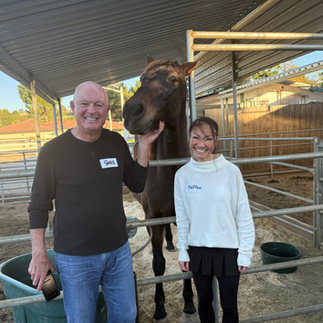 Two guests smiling beside a horse inside the covered arena at Rockin’ T Ranch during the Gleason Tennis Autumn Festival.