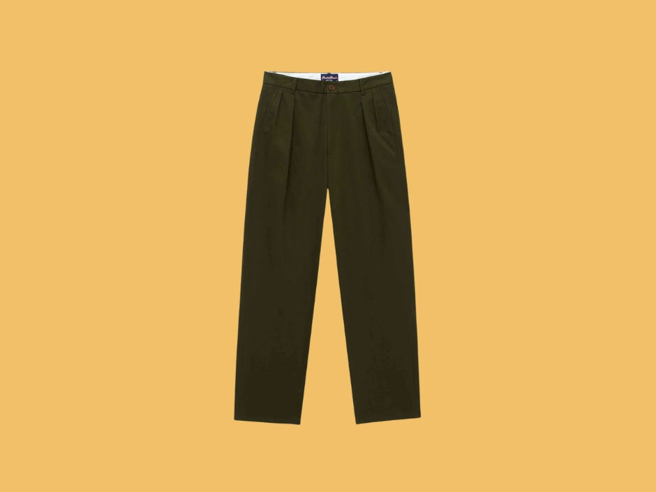 Dark green pants with pleats displayed against a mustard yellow background. A small label is visible at the waistband.