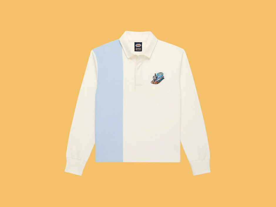 White and blue long-sleeve polo shirt with a cartoon train patch on the chest, set against a solid orange background.