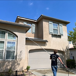 Cleaning second-story residential home windows with a long water-fed pole system.
