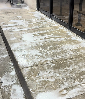 Cleaning solution and foam soaking into a concrete surface next to a glass pool fence.