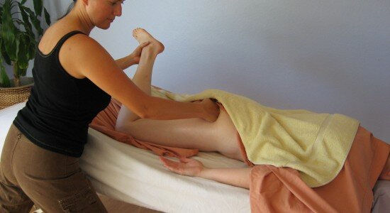 massage therapist applying pressure to draped client's glute muscles