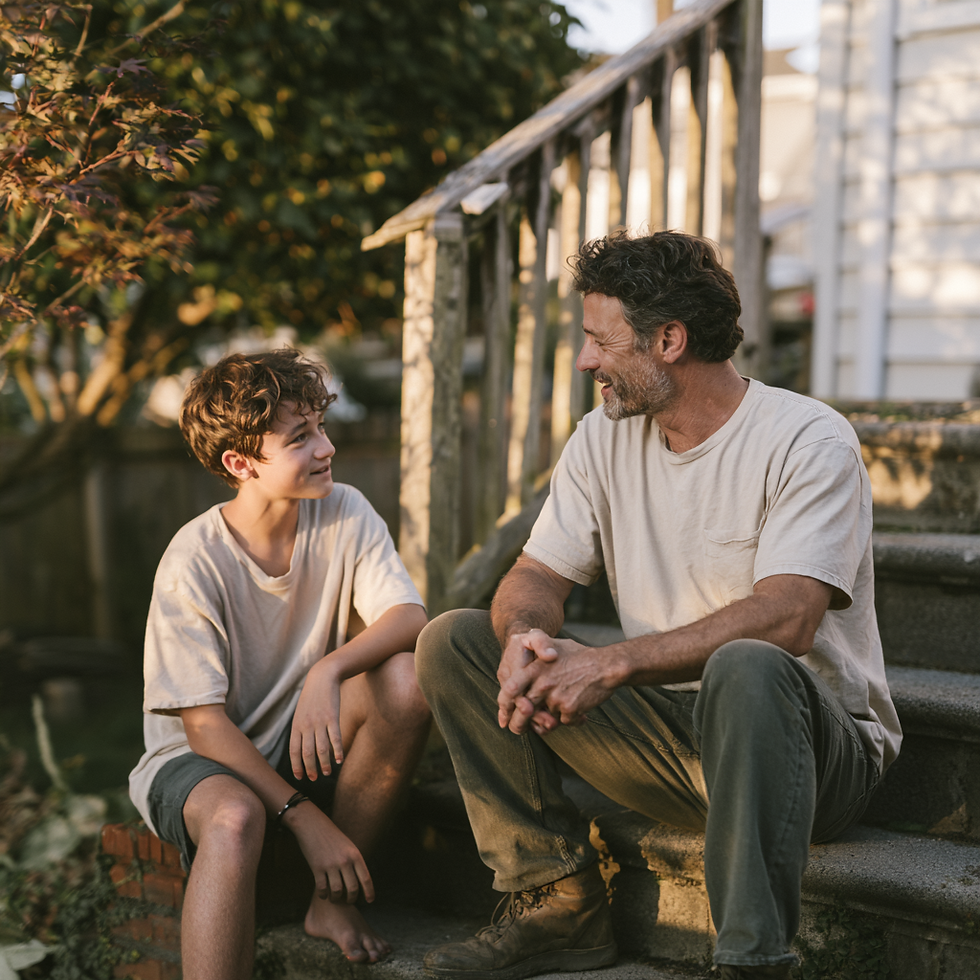 A father and teenage son sit together on outdoor steps, talking calmly in the warm evening light.
