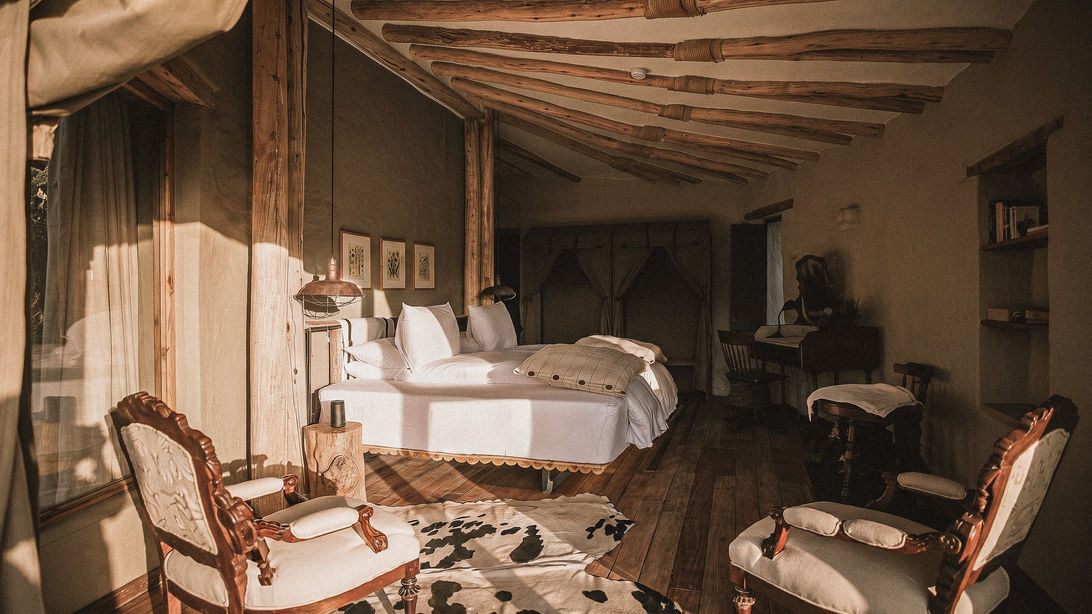 Chambre double du Pavillon Pirca au Puqio : fauteuils brodés d'époque, bureau d'écrivain et murs en adobe sous plafond de bois sauvage, sélection Graine de Voyageur.