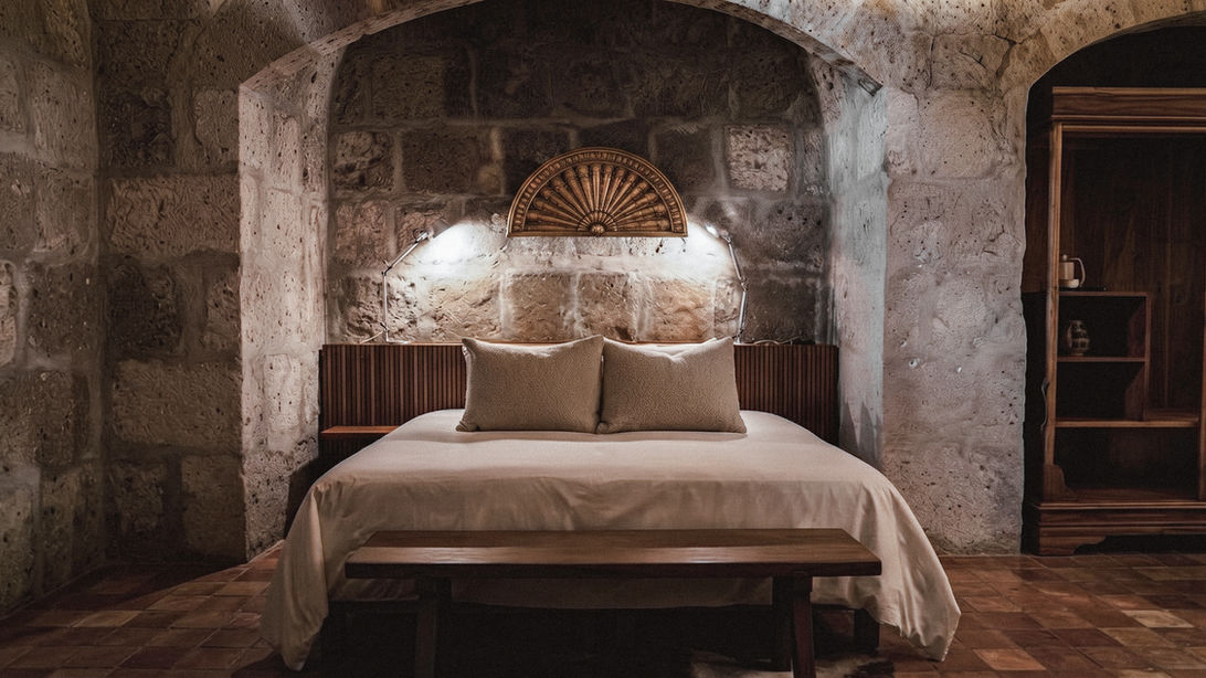 Hôtel de luxe Palacio Guaqui à Arequipa : Lit de la Suite Deluxe abrité sous une alcôve historique en pierre de sillar, sélectionné par l'agence Graine de Voyageur au Pérou.
