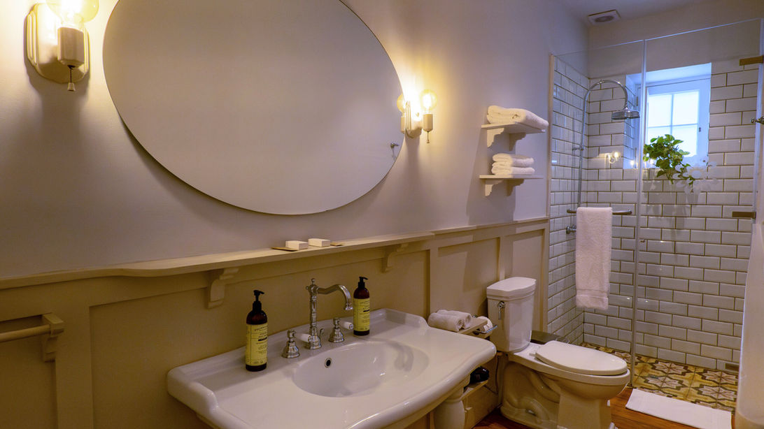 Salle de bain de charme à la Villa Barranco avec grand miroir ovale, lavabo sur pied, toilettes et douche carrelée style métro.