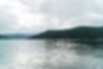 2 paddlers on SUP boards on the Salish Sea. It is a cloudy day with hills in the background.