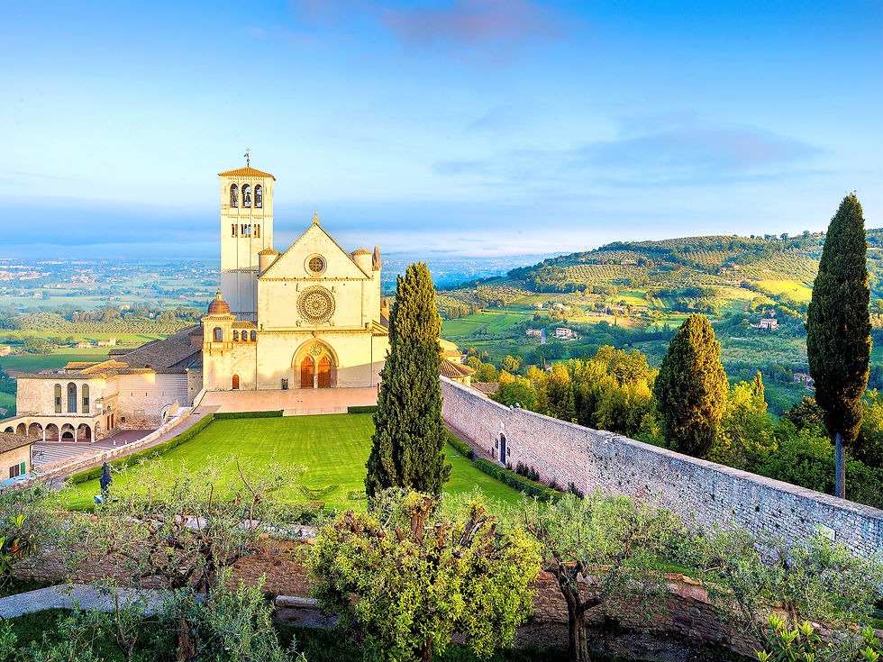 Basilika in Assisi mit Uhrturm, umgeben von grünen Feldern und Zypressen, unter blauem Himmel. Friedliche, ländliche Stimmung.