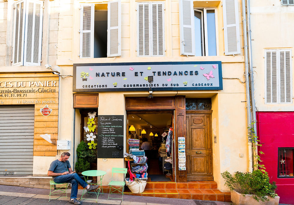 Geschäftsfassade mit dem Schild "NATURE ET TENDANCES". Mann sitzt an grünem Tisch. Innenstadtumgebung mit beigen Hausfassaden.