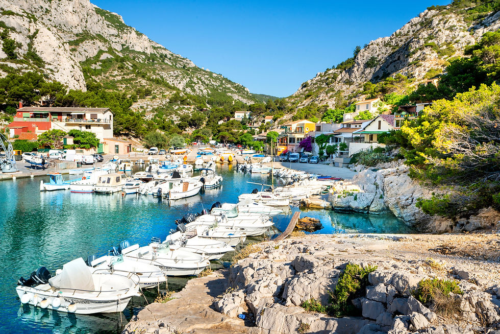 Calanque de Sormiou, Boote im malerischen Hafen vor farbenfrohen Häusern und bewaldeten Hügeln. Klare blaue Himmel und ruhiges Wasser erzeugen eine friedliche Stimmung.