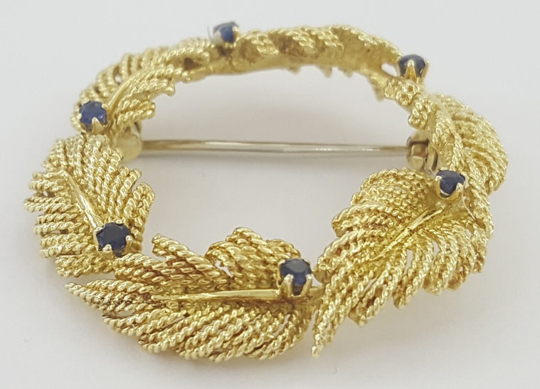 Tiffany gold and sapphire brooch on off-white background.