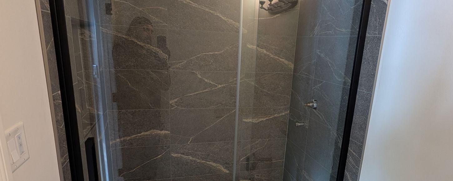 Completed shower glass enclosure in a Regina bathroom by B-Flex Services with dark tile walls, glass door, and finished renovation layout.